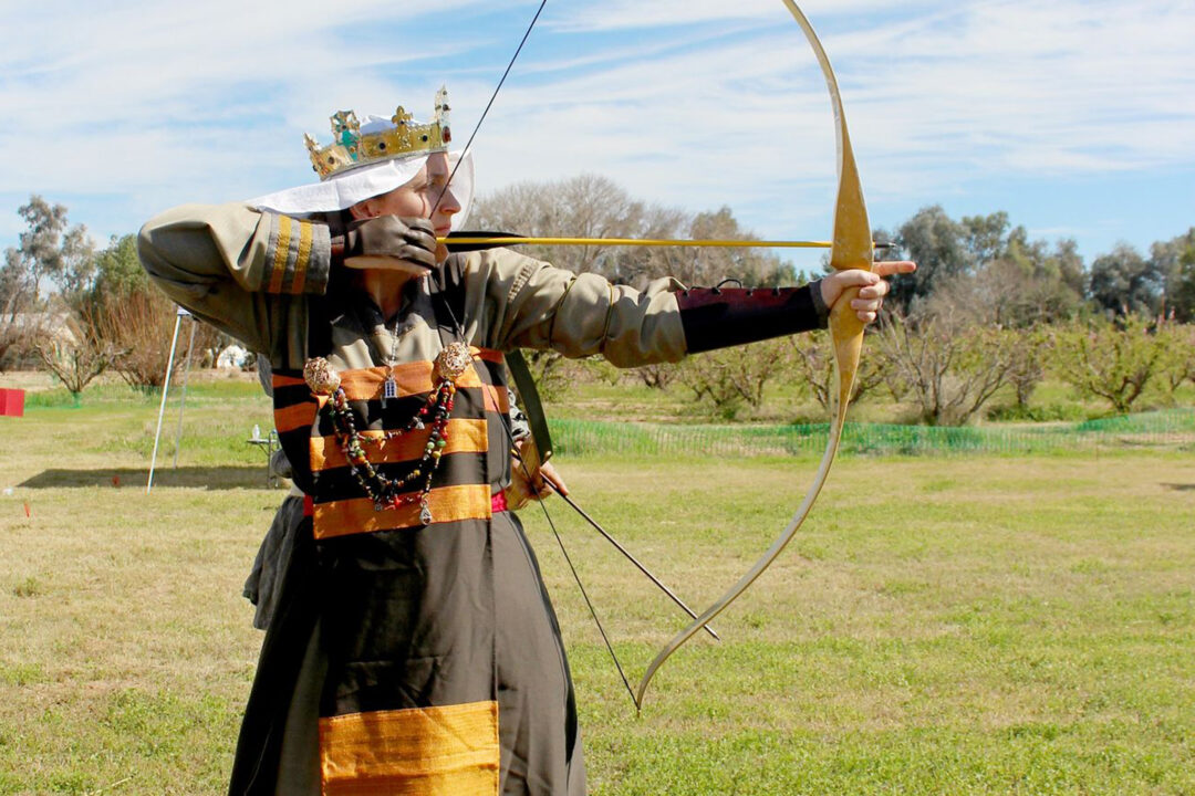 A feminine presenting Royal Peer shooting archery in a field